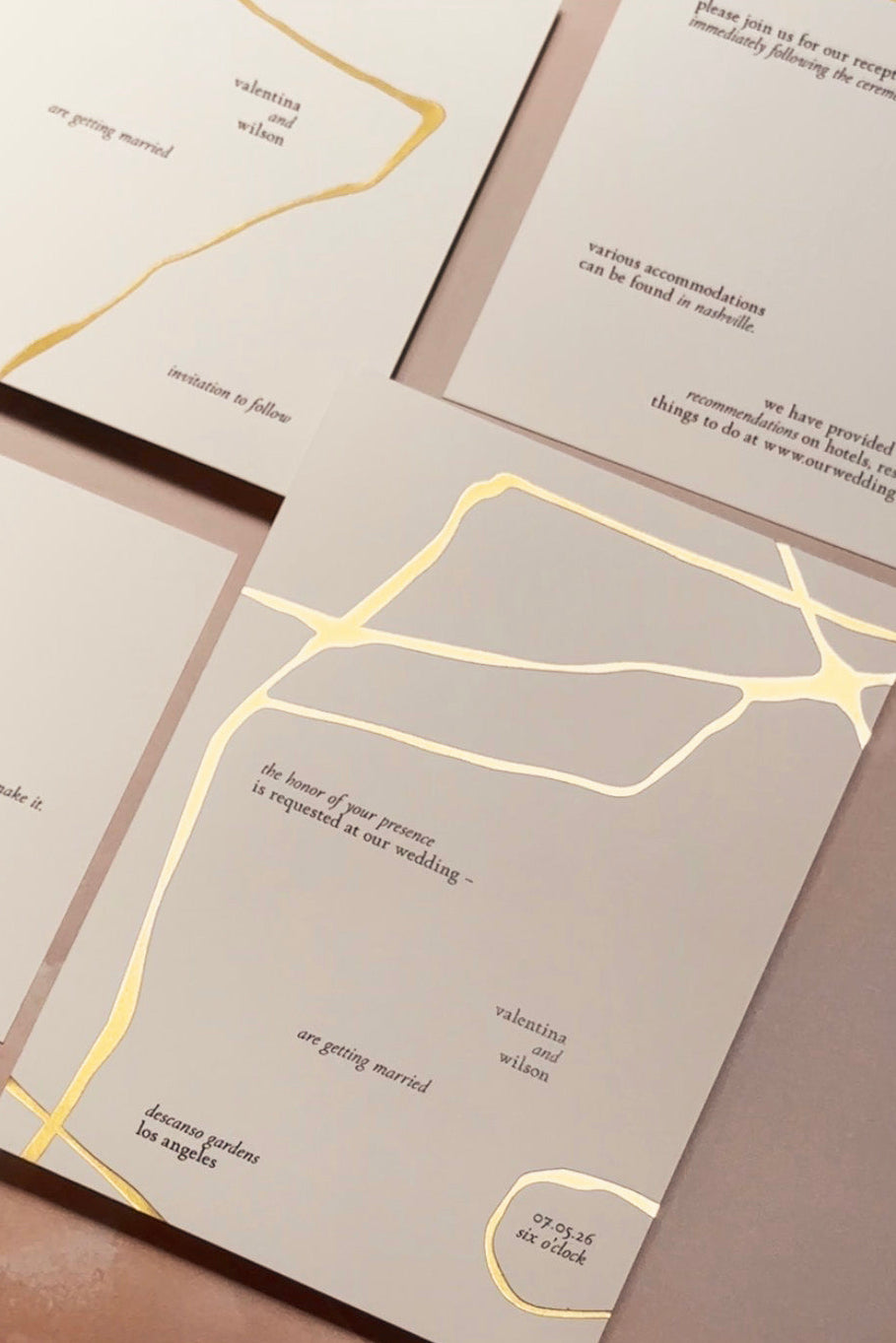 Flatlay of white wedding stationery with gold foiled kintsugi lines on a light pink background