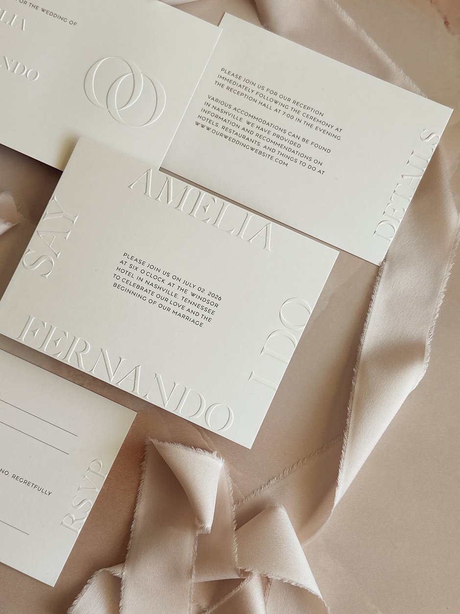White blind embossed wedding staionery on a light pink background and light pink silk ribbon